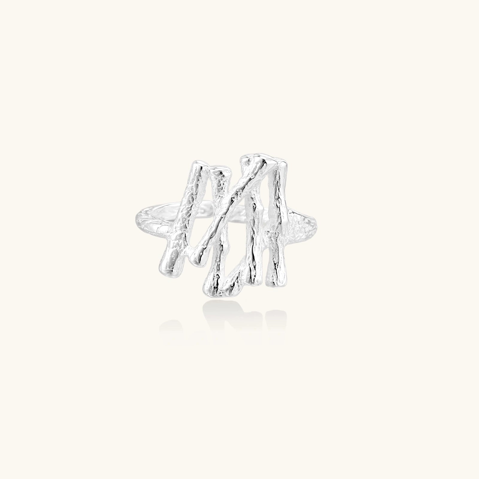 Sculptural sterling silver ring with organic branch design and textured surfaces on cream background